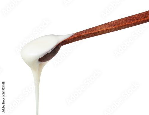 side view of natural organic white honey pouring from little wooden spoon closeup isolated on white background