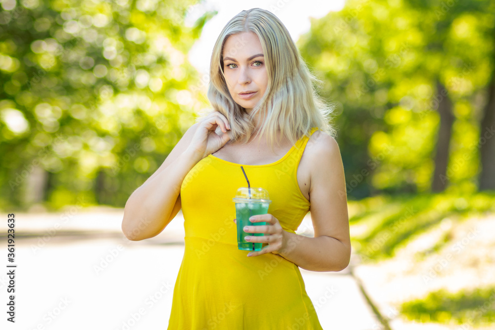 Blonde woman in short yellow dress drinking coctail in park Blonde woman in short yellow dress drinking coctail in park