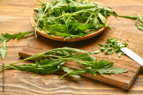 Plate with fresh arugula and cutting board on wooden background