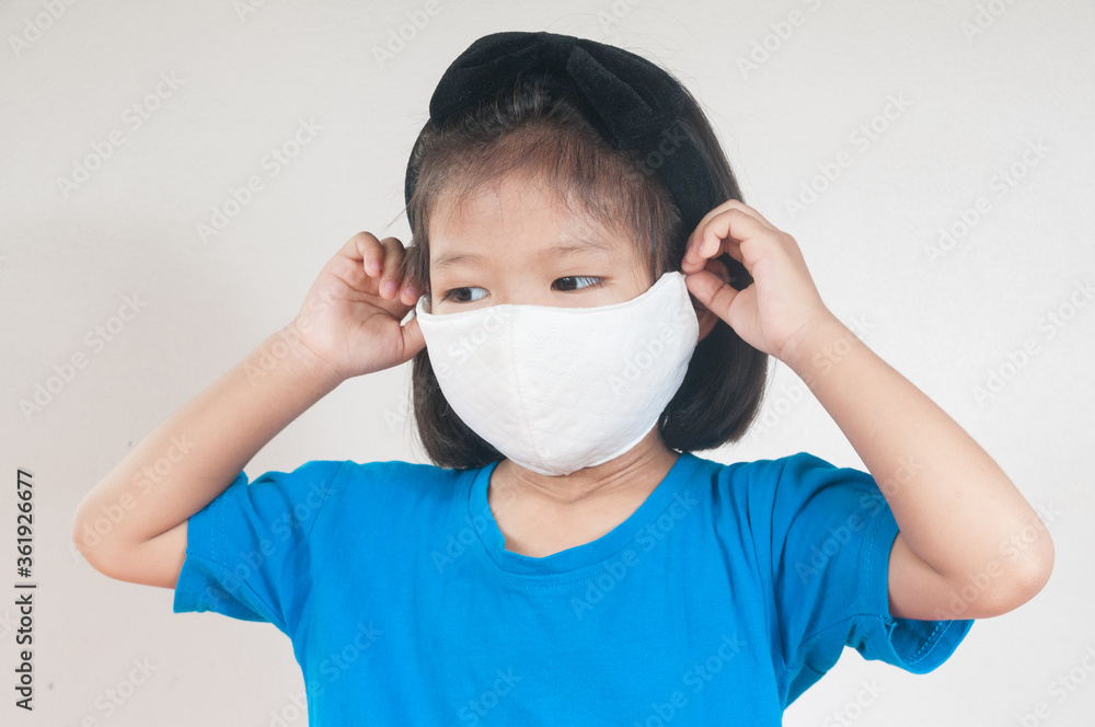 Asian child Girl or kids in blue Shirt wearing cloth mask to protect Covid 19 virus infection as medical safety prevention concept against white background. Asian child Girl or kids in blue Shirt wearing cloth mask to protect Covid 19 virus infection as medical safety prevention concept against white background.