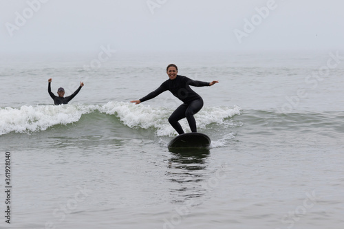 Fototapeta Young multiracial African American lady with amazing smile, freckles & frizzy hair & an Asian Japanese Surf Instructor having a surf lesson together in Chiba, Japan They are wearing black wetsuits