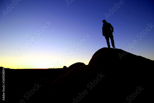 Man standing on top of a hill watching sunset in sillhoutte