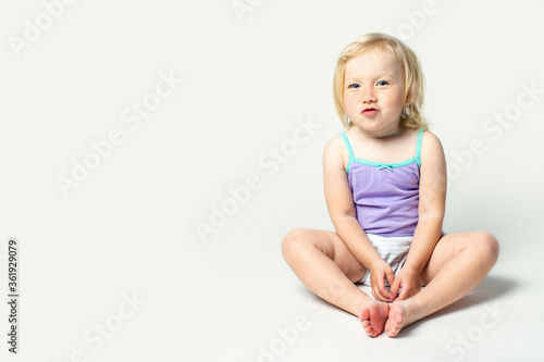 Beautiful cute little baby makes a bow with a sponge in a shirt and panties on a white background