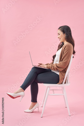Beautiful and happy woman working with a laptop, isolated over pink background