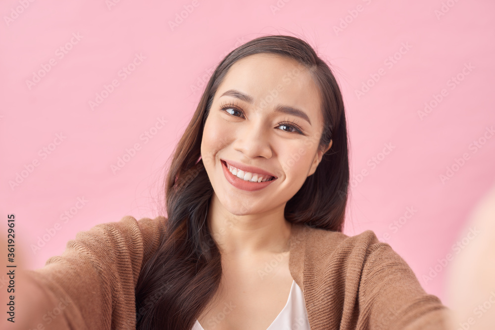 Studio portrait of beautiful woman smiling with white teeth and making selfie, photographing herself over pink background Studio portrait of beautiful woman smiling with white teeth and making selfie, photographing herself over pink background