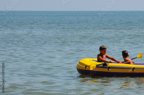 Boys are sailing on a boat on the sea. The older brother rides the younger brother on an inflatable boat on the water. Friends are drifting on the sea in a boat. Friendship, mutual assistance. © BetterPhoto