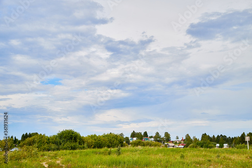 Beautiful landscape with blue sky, white clouds, green field and village on the background. © keleny