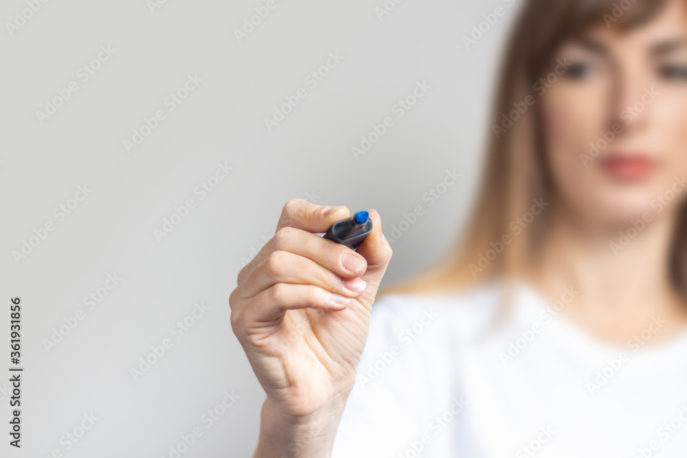 Young woman holds a blue marker and writes something on a light background. Banner Young woman holds a blue marker and writes something on a light background. Banner