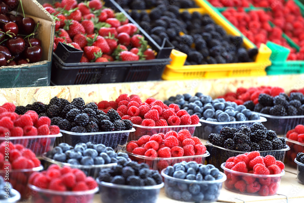 Raspberries, blueberries and blackberries on a market in plastic bowls. Fruits pattern.