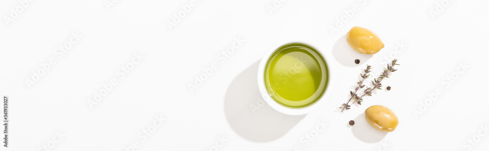 top view of olive oil in bowl near green olives, herb and black pepper on white background, panoramic orientation top view of olive oil in bowl near green olives, herb and black pepper on white background, panoramic orientation
