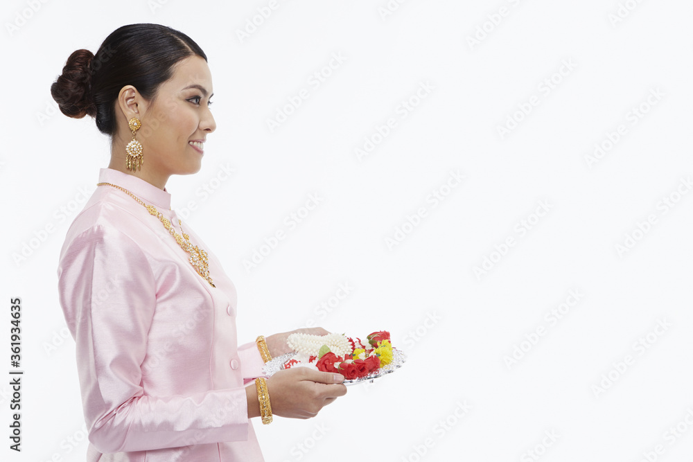 Woman in traditional clothing holding up a tray with Thai flower garlands Woman in traditional clothing holding up a tray with Thai flower garlands