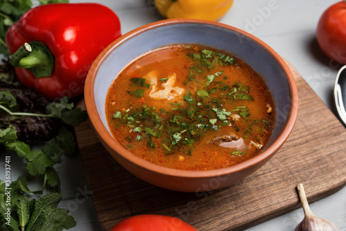 a plate of borsch with a spoon and a hand. chilli scattered around. gray wooden background