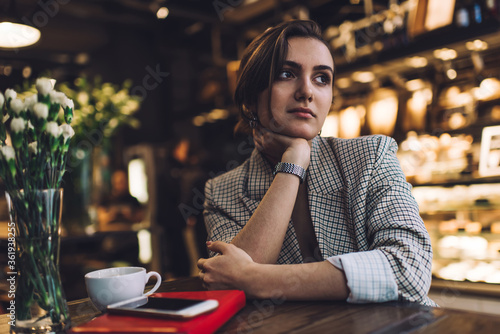 Contemplative hipster girl thoughtful looking away thinking about education learning during pastime in coffee shop  pensive female student in smart casual apparel feeling pondering at cafeteria
