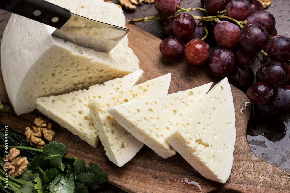 Slices of triangular cheese on a board. There are a lot of vegetables and grapes around. close-up top view. Georgian cuisine