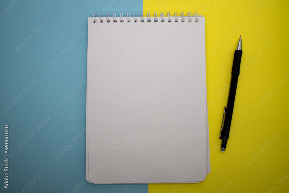 Notepad with kraft paper, pen, on a yellow and blue background. Workspace concept. Top view, copy space, layout, flat lay Notepad with kraft paper, pen, on a yellow and blue background. Workspace concept. Top view, copy space, layout, flat lay