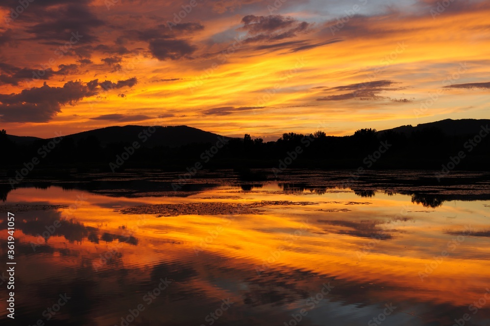 Lake, golden light at dusk. With reflection on the water surface. Beauty orange colored clouds . Dubnica, Slovakia.
