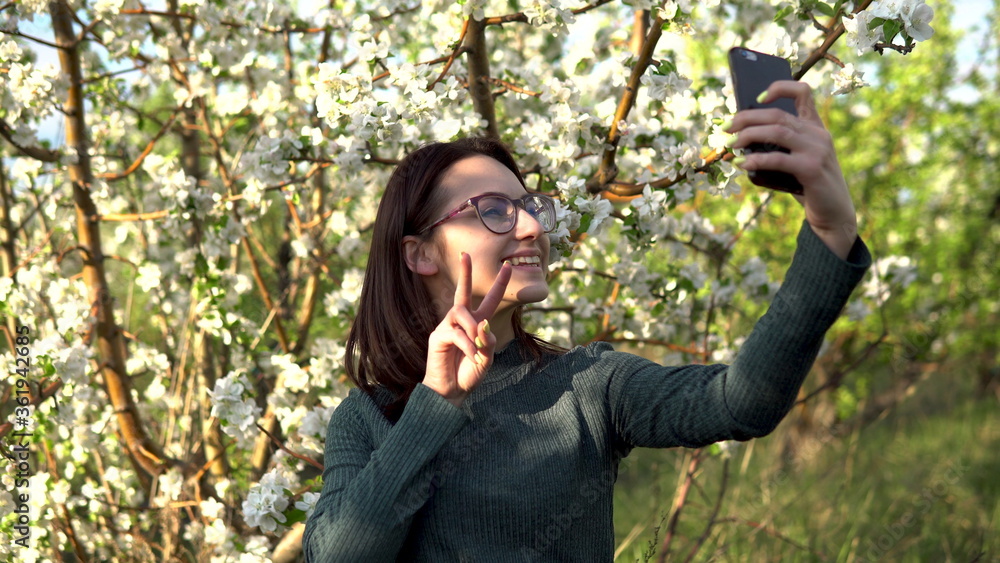 A young woman photographs herself against the backdrop of an apple tree. Girl in the blooming garden. A young woman photographs herself against the backdrop of an apple tree. Girl in the blooming garden.