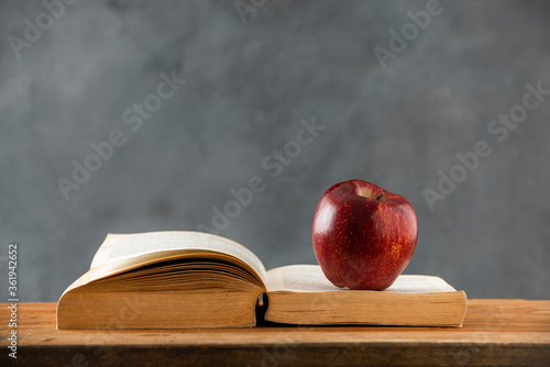 on the wooden table, an open book with a red apple on it. copy space photo