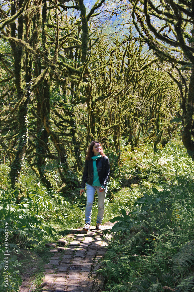 photo of a girl, walking along the trail path, through Dead boxwood forest to Mirveti Waterfall in the mountains of Georgia at sunny day, in spring.