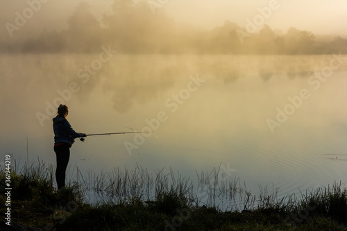 Girl fishermen at dawn. Girl Fishermen in the morning fog on the river bank. Fishermen with fishing rods. Autumn fishing. Morning fog at sunrise. Autumn morning fog.