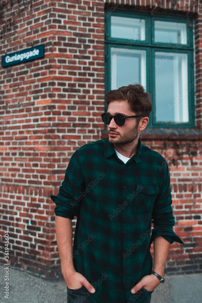 Young man in sunglasses with hands in pocket standing on urban street, Copenhagen, Denmark Young man in sunglasses with hands in pocket standing on urban street, Copenhagen, Denmark