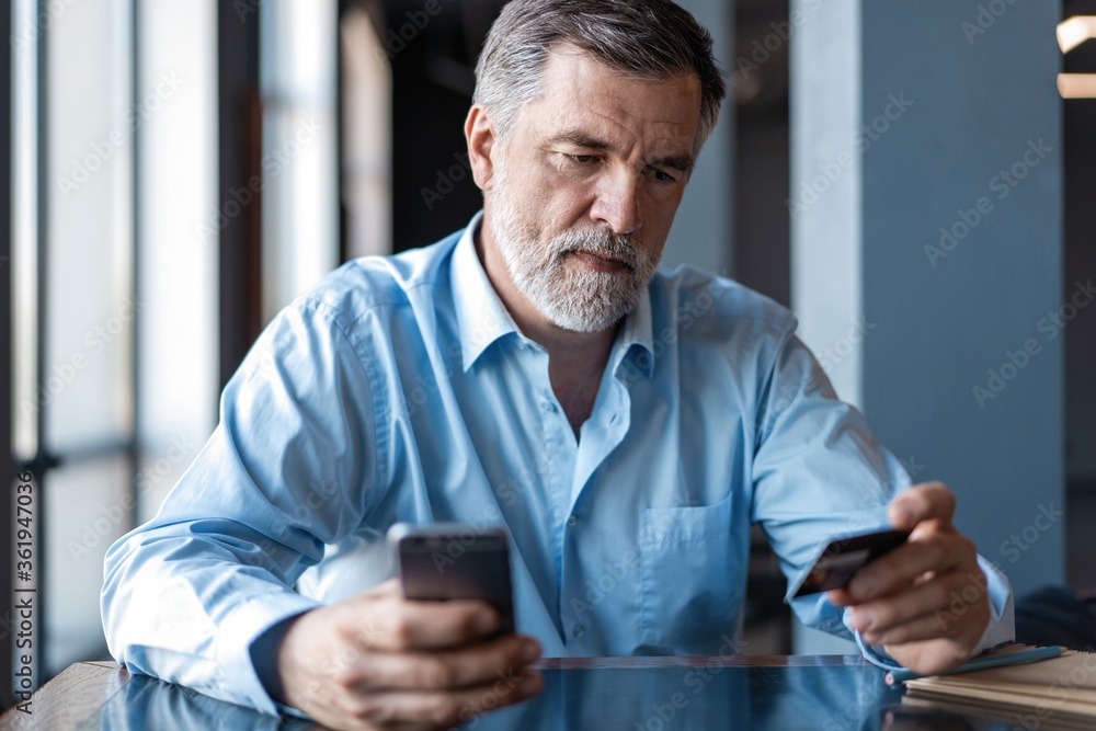 Fototapeta premium Online Payment on Smartphone by Mature Man. Handsome mature business leader sitting in a modern office