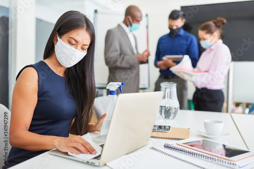 Business Frau mit Mundschutz beim Arbeitsplatz desinfizieren