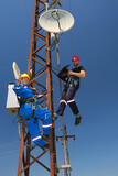 Two electricians in protective workwear install telecommunications antenna system