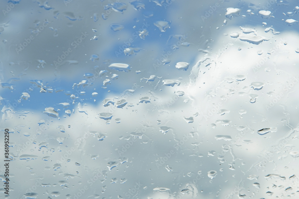 Raindrops on the window glass. Clear blue sky with white clouds. Blurred background. Raindrops on the window glass. Clear blue sky with white clouds. Blurred background.