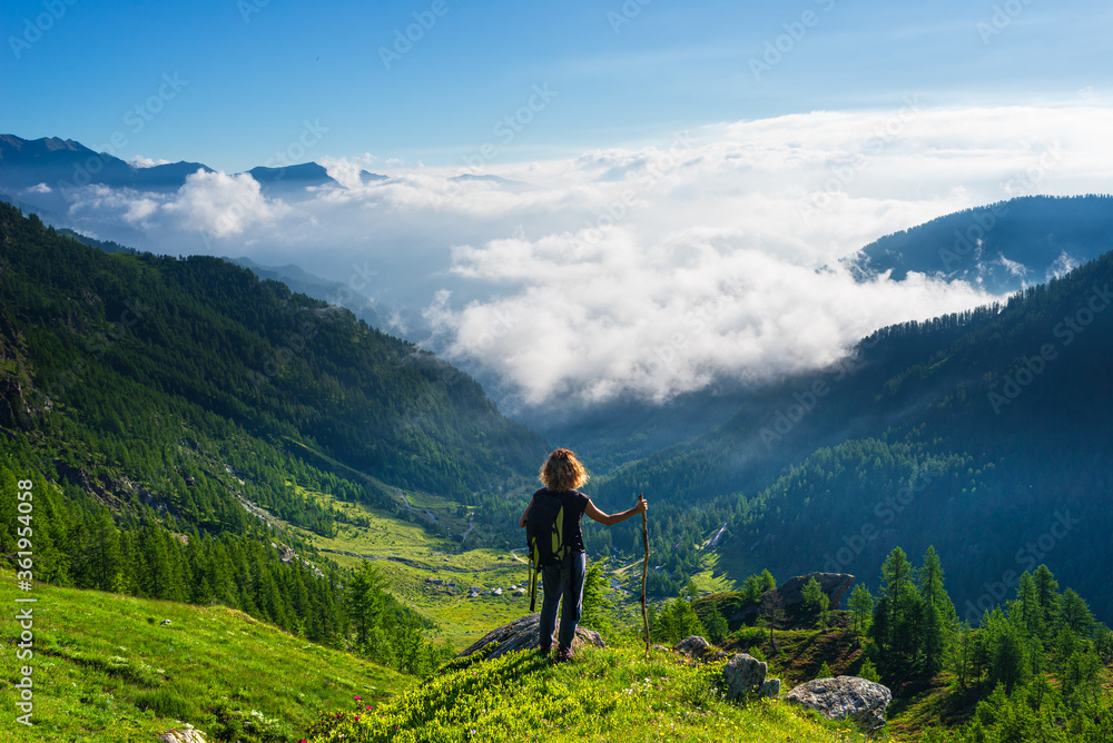 Woman resting on mountain top, looking at view dramatic landscape clouds over the valley, clear blue sky. Summer activity fitness wellbeing freedom success.