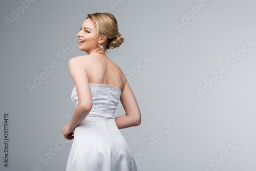 cheerful young bride in white wedding dress isolated on grey