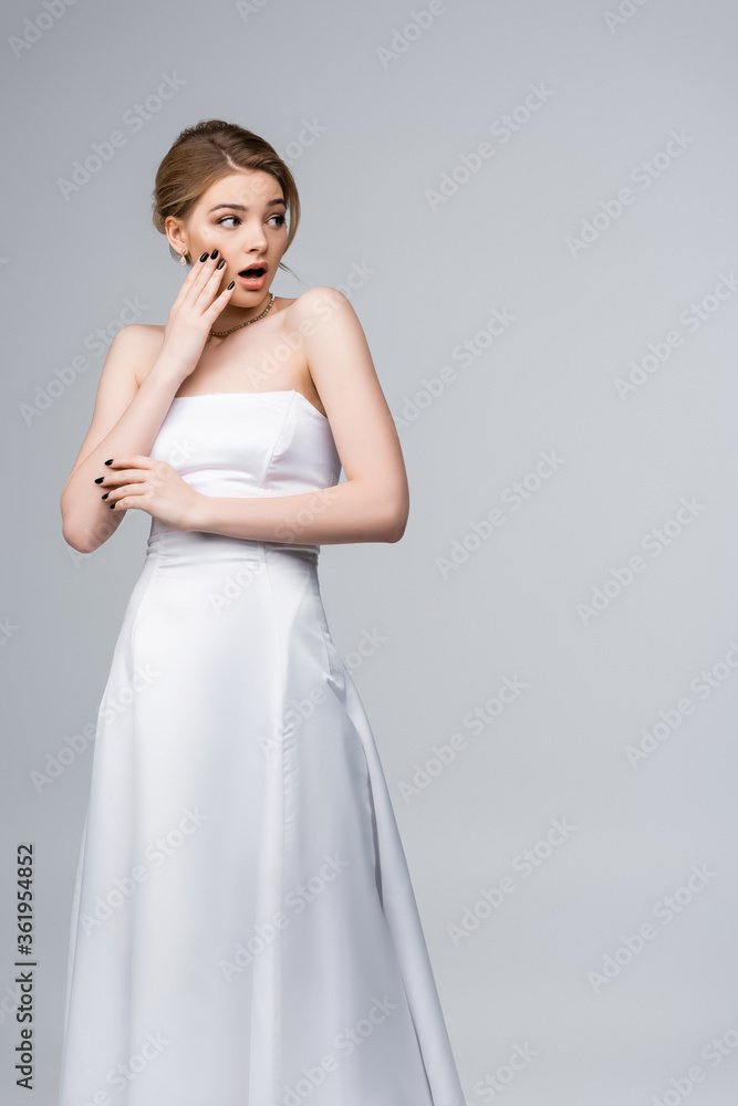 shocked bride in wedding dress looking away and touching face isolated on grey shocked bride in wedding dress looking away and touching face isolated on grey