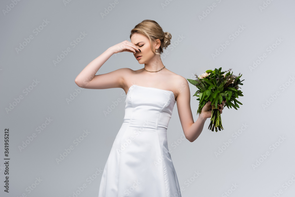 displeased bride in white wedding dress touching nose while holding smelly flowers isolated on grey displeased bride in white wedding dress touching nose while holding smelly flowers isolated on grey