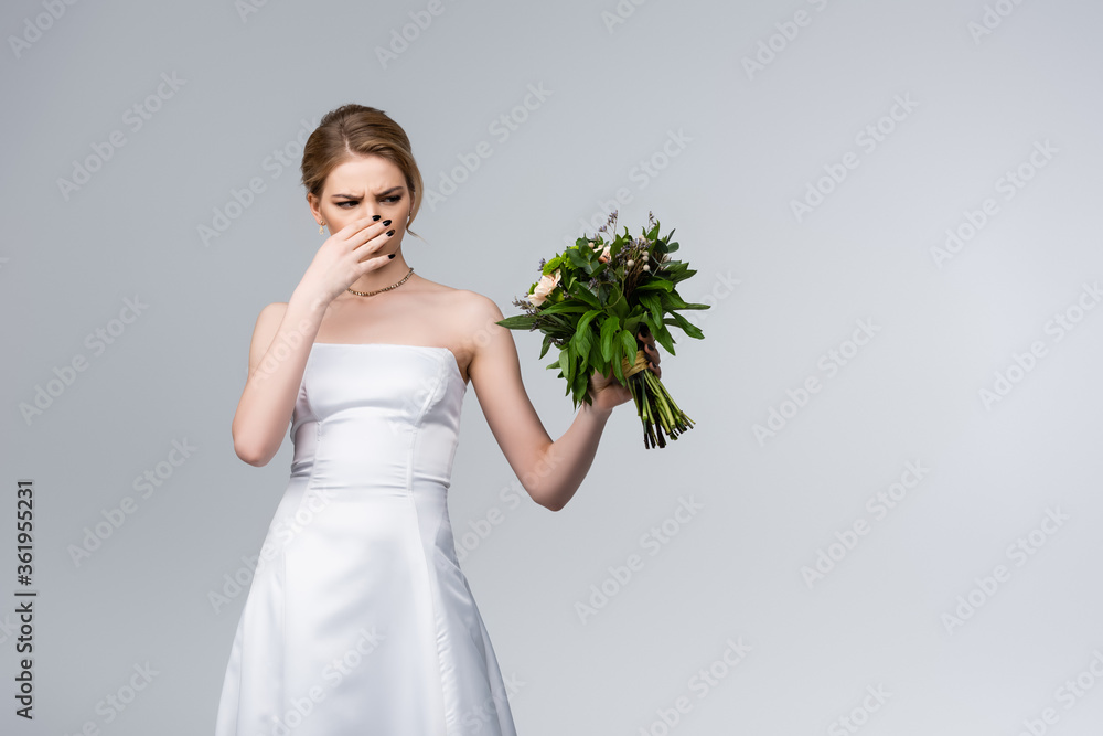 bride in white wedding dress touching nose while holding smelly flowers isolated on grey bride in white wedding dress touching nose while holding smelly flowers isolated on grey
