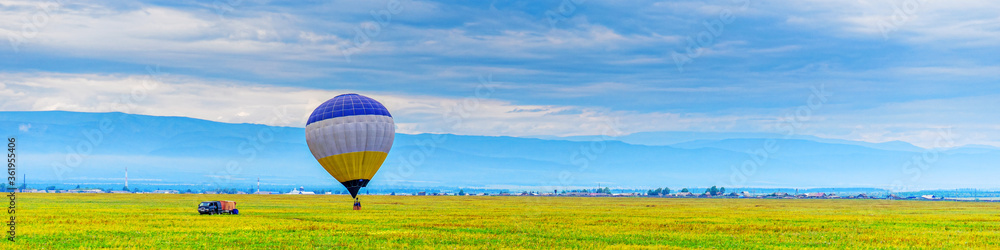 Picturesque summer panoramic landscape of mountain valley, green grass and cloudy sky with air balloon before flight. Banner for productive and extreme leisure, adventure themes with space for text