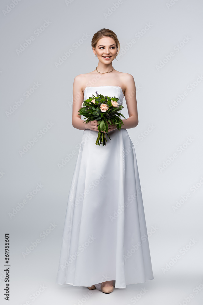 smiling bride in white wedding dress holding bouquet of flowers on grey smiling bride in white wedding dress holding bouquet of flowers on grey