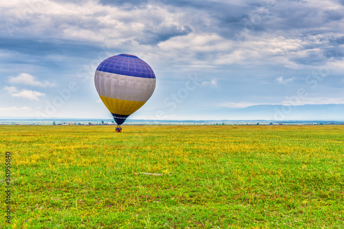 Picturesque summer landscape of mountain valley, green grass and cloudy sky with air balloon before flight. Misty morning, Tunkinsky district, Buryatia, Russia