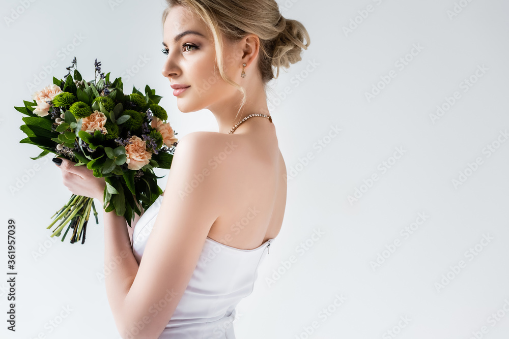 attractive bride in wedding dress holding flowers on white