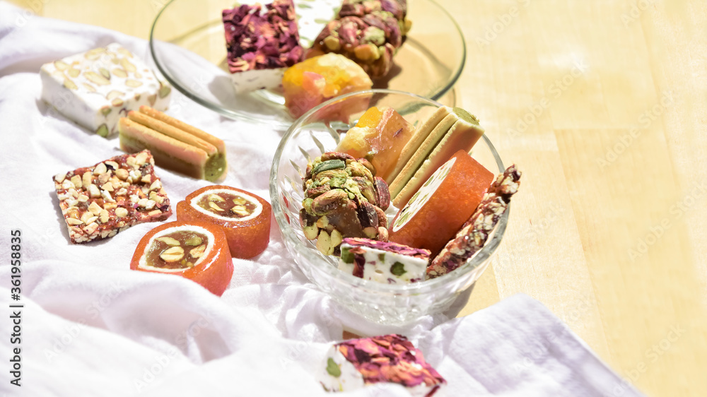 Still life with different Lebanese sweets types (made from honeyed orange paste, dried fruits, roasted almonds, pistachios and rose petals) on a recycled wooden table covered with a white cloth