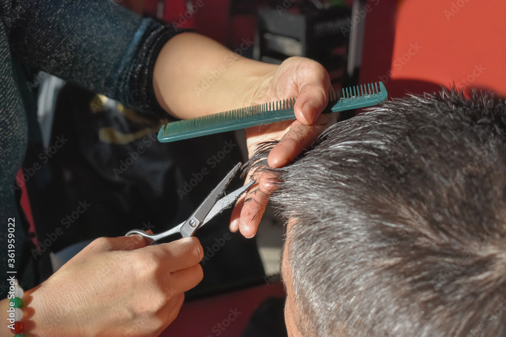 Skillful hands of a hairdresser cutting and combing the bangs of a middle-aged gray-haired client. Hair care