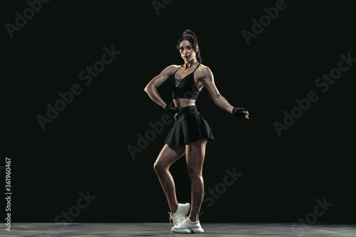 Beautiful young female athlete practicing on black studio background  full length portrait. Sportive fit brunette model posing confident. Body building  healthy lifestyle  beauty and action concept.