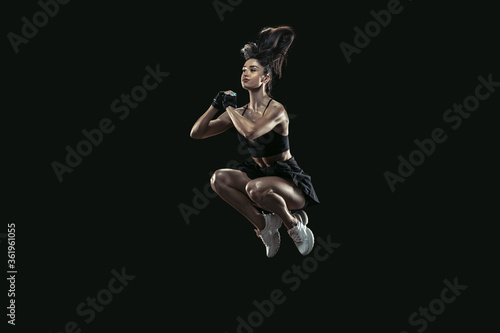 Beautiful young female athlete practicing on black studio background, full length portrait. Sportive fit brunette model in high jump. Body building, healthy lifestyle, beauty and action concept.