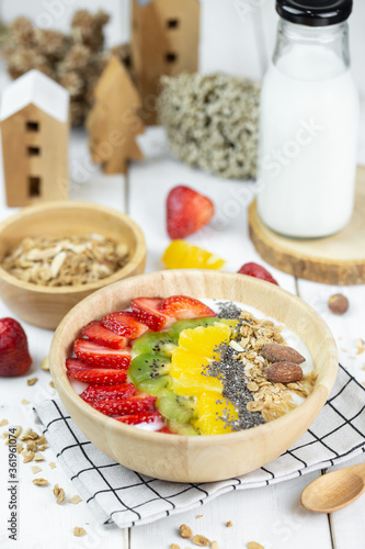 One big bowl of natural yogurt with strawberry, kiwi, almond, pineapple serve on wood table and milk.