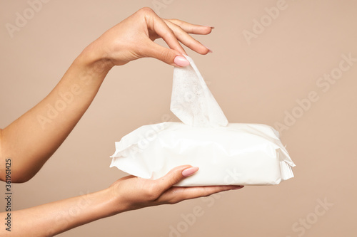 Hygiene. Female hands takes wet wipes from white packaging on a beige background. Daily hygiene for the prevention of viral and bacterial infections.