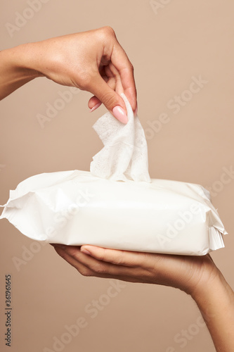 Hygiene. Female hands take wet wipes from white packaging on a beige background. Daily hygiene for the prevention of viral and bacterial infections.
