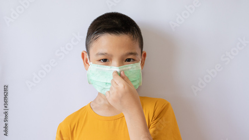 An Asian boy wears a COVID-19 anti-dust mask and is dustproof. Lift your finger and squeeze your mask. White background in the house