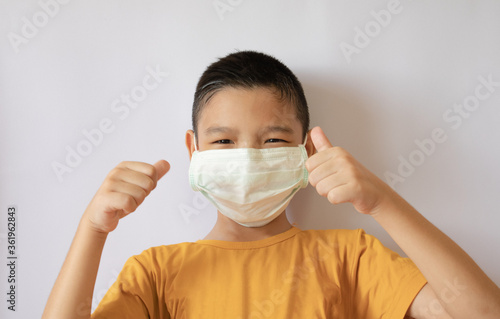 A thai boy wearing a COVID-19 anti-virus mask and dust is pretending to raise his thumb. white background in the house