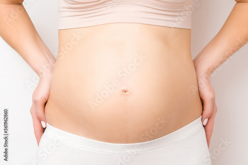 Young woman showing naked big belly isolated on gray background. Body shape. Emotional loving pregnancy time - 20 weeks. Baby expectation. Love, happiness and safety concept. Closeup. Front view. © fotoduets