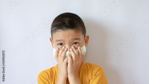 An Asian boy wears a COVID-19 anti-dust mask and is dustproof. Raise his hand and cover his face. White background in the house