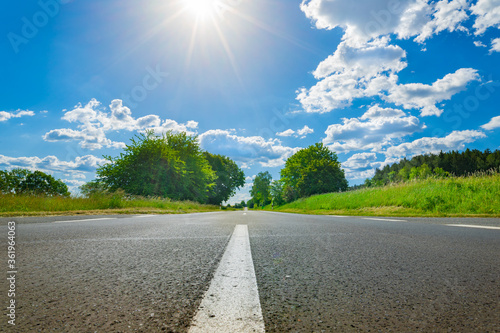 Asphalt road with white dividing lines, landscape and cloudy sky with sun